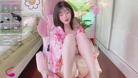 Media: Video of a young East Asian woman with shoulder-length black hair, wearing a pink floral kimono, sitting on a pink gaming chair.