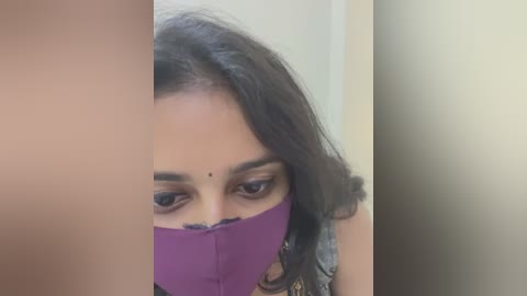 Media: Video of a woman with dark brown skin, long dark hair, wearing a purple mask, partially covering her face, with a small dot on her forehead.