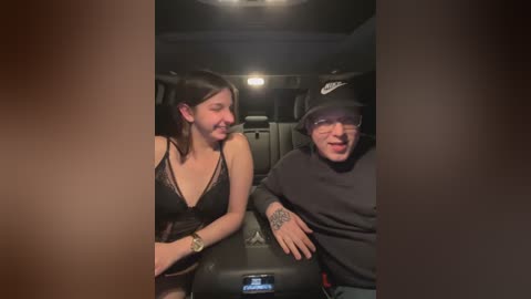 Media: A video of a young woman with long dark hair in a black lace top and a man in a black beanie and glasses, sitting in a dark car interior with dim lighting.