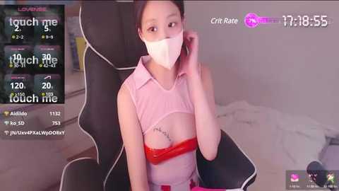 Media: Video of a young Asian woman in a pink tank top with a red lace bra visible, sitting in a gaming chair, wearing a face mask, surrounded by streaming app interface.