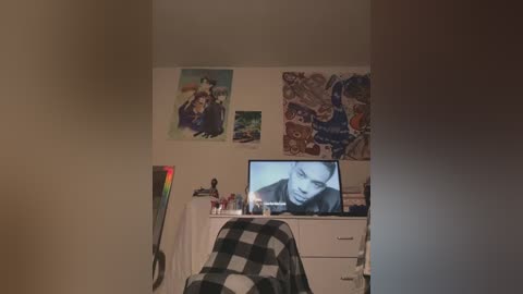 Media: A video of a dimly lit bedroom with a white dresser, a TV showing a black-and-white image, a black-and-white checkered blanket, and various posters on the wall.