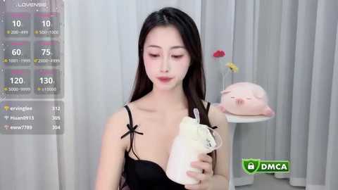 Media: Video of an East Asian woman with long black hair, fair skin, wearing a black lace bra, holding a white chicken. Background features a digital screen displaying livestream stats and a pink plush toy.