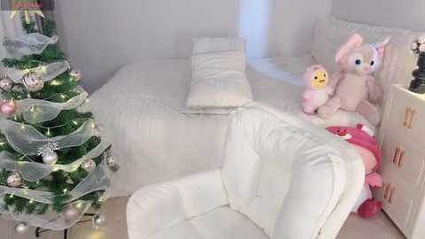 Media: A video of a cozy, minimalist bedroom with a white bed, plush toys, a pink bunny, and a decorated Christmas tree in the corner.