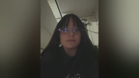 Media: A video of a young person with long black hair, wearing round blue-tinted glasses and a dark shirt, captured from a low angle inside a narrow space, creating a claustrophobic effect.