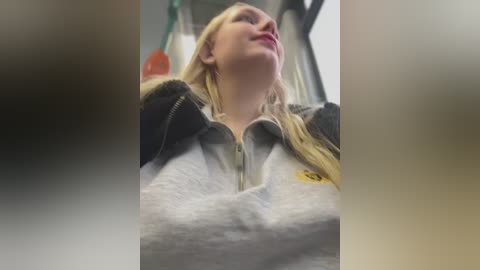 Video of a blonde woman with fair skin, wearing a gray hoodie with a yellow logo, leaning back with eyes closed, taken from a low angle.