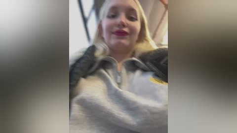 Media: A blurred video shows a blonde woman with fair skin, wearing a grey and white jacket with a fur trim, smiling inside a train.