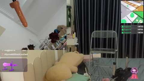 Media: Video of a virtual reality scene featuring a person in a VR headset, kneeling on a beige couch, surrounded by stuffed animals, a white chair, and a dark curtain background.