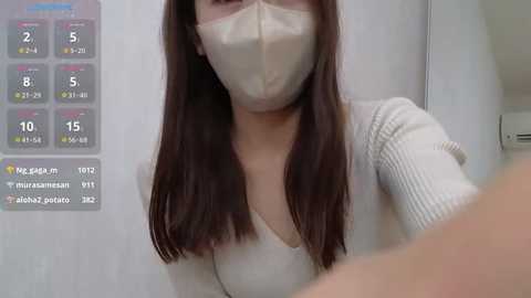 Media: A video shows an Asian woman with straight, dark brown hair, wearing a beige face mask, and a ribbed, off-white top. In the background, there's a temperature chart displaying 2 degrees Celsius.