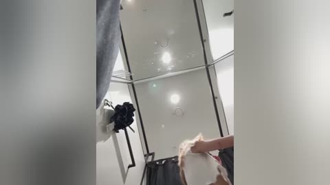 Media: Video of a modern, white-tiled bathroom with a mirror, a white robe hanging on a hook, and a hand holding a towel.