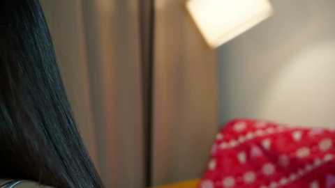 Media: Video of a cozy, dimly lit bedroom with a soft, glowing lamp illuminating a red blanket with white polka dots, contrasting against a muted grey wall and a wooden wardrobe.