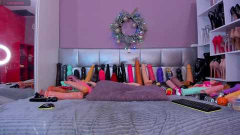 Media: A video of a vibrant, cluttered bedroom with a plethora of colorful sex toys on a bed, purple wall, and a festive wreath.