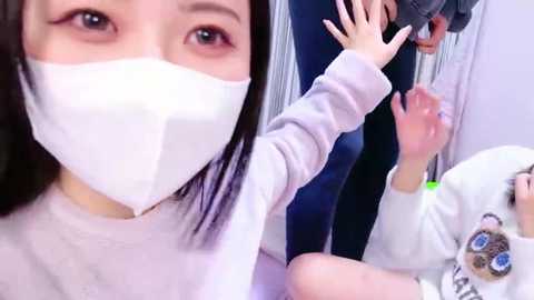 Media: A video shows an Asian woman with long black hair and a white mask, holding a black gun to a young girl's head in a white room. The girl wears a white sweater with a cartoon character.