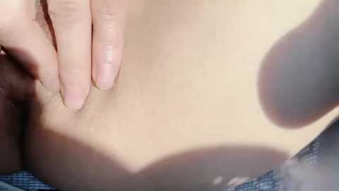 Video of a close-up of a light-skinned person's lower abdomen, with a hand gently touching the skin. The background is blurred, with a faint, out-of-focus shadow. The texture of the skin appears smooth and unblemished.