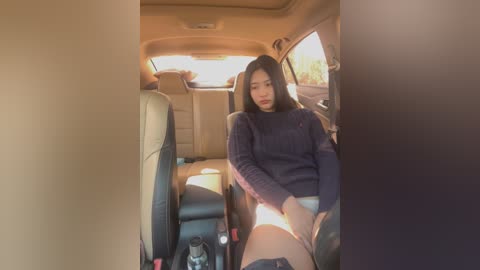 Media: A video of an Asian woman in a navy sweater and white panties, seated in a beige-carpeted car with sunlight streaming in.