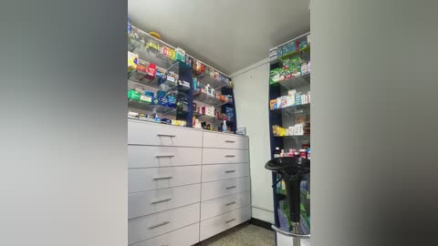 Media: Video of a modern, organized medicine cabinet with white drawers and shelves, stocked with colorful, neatly arranged pharmaceuticals and toiletries. A black trash can is partially visible in the foreground.