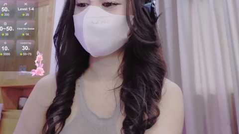 Media: A video of an Asian woman with long black hair, wearing a white surgical mask and a grey tank top, indoors, with a digital health monitoring display in the background.