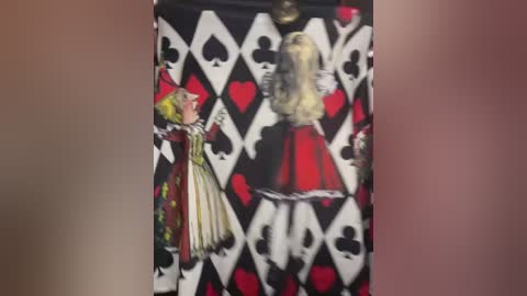 Media: A video of a woman's back, clad in a red and white dress with black hearts and spades, standing against a black and white diamond-patterned wall.