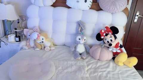 Media: Video of a whimsical, plush-filled bedroom featuring a Minnie Mouse doll, Winnie the Pooh, and stuffed animals on a white bed, with a wooden headboard and pastel decor.