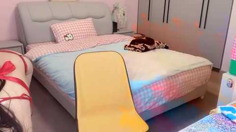 Media: Video of a colorful, cartoon-themed bedroom with a light gray upholstered bed, yellow chair, checkered bedding, and a wall adorned with decals.