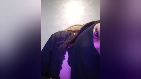 Media: A video of a person's upper body, wearing black clothing, partially obscured by a textured, light gray background with a soft, glowing light source.