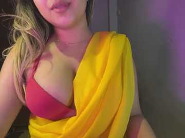 Media: Video of a light-skinned woman with long, wavy blonde hair, wearing a bright red bra and a yellow saree, with a purple wall in the background.