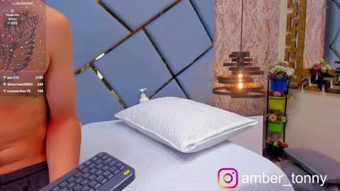 Media: Video of a shirtless man with light skin, sitting at a desk with a white pillow, surrounded by a modern, geometrically patterned wall and colorful decor, with a \"amber_tonny\" watermark.