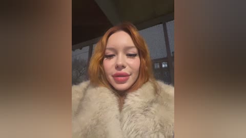 Media: Video of a young Caucasian woman with fair skin and shoulder-length, light brown hair, wearing a beige fur coat, puckering her lips in a playful manner. Background features a blurred, modern indoor setting with wooden ceiling beams and a large window.