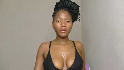 Media: Video of a young African woman with medium-dark skin, wearing a black lace bra, her hair styled in a large, voluminous afro. She stands against a plain, beige wall.