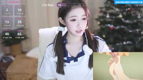 Media: Video of a young Asian woman in a white sports outfit with twin braids, sitting in a chair, wearing a stethoscope, with a blurred Christmas tree in the background.