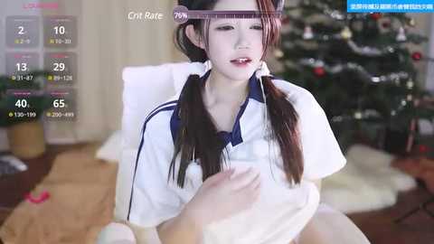 Media: A video of an Asian woman with long black hair in twin braids, wearing a white school uniform, sitting on a couch beside a decorated Christmas tree.