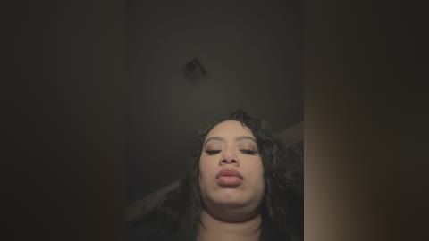 Video of a young Black woman with curly hair and full lips, captured from a low angle, with a dimly lit, dark background.