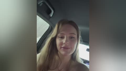 Media: Video of a young Caucasian woman with long, straight, light brown hair, fair skin, and a slim physique, seated in a car with her head tilted slightly to the right.