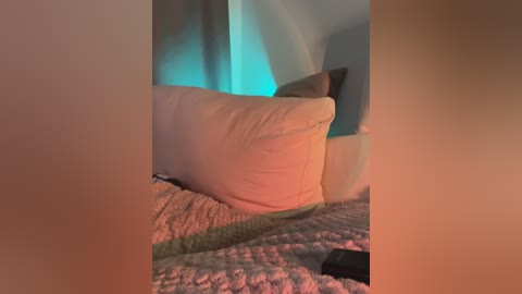 Video of a cozy, dimly-lit bedroom corner with a beige cushion, a beige blanket, and a muted teal wall, creating a soft, warm ambiance.