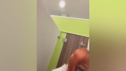 Video of a modern, minimalist bathroom with a lime green accent wall and wooden vanity, featuring two white hooks. The image is slightly blurry.