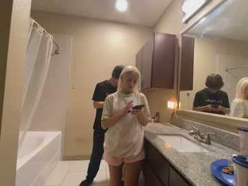 Media: A video of a young blonde woman in a white t-shirt and pink shorts taking a selfie in a modern bathroom with beige walls and a granite countertop.