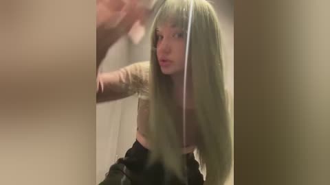 Media: Video of a young woman with long, platinum blonde hair and a light complexion, wearing a beige crop top and black skirt. She has a startled expression, and her hair is partially caught in a doorway.