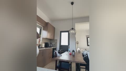 Media: Video of a modern, minimalist kitchen with light wooden cabinets, a stainless steel sink, a microwave, and a small dining area with a wooden table and chairs.