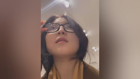 Media: Video of a young Asian woman with straight black hair, glasses, and a beige scarf, smiling, taken from a low angle.