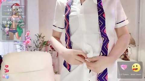 Video of a person wearing a white shirt with purple tie, adjusting the tie. Background features a pink wall with a poster and a white couch.