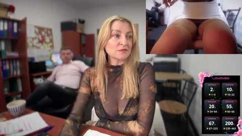 Media: Video of a blonde woman in a semi-transparent black top and sheer black tights, seated at a desk in an office, with a close-up of her exposed buttocks in the background.