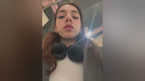 Media: Video of a young woman with fair skin, wearing a black bra and gray jacket, taking a selfie indoors.