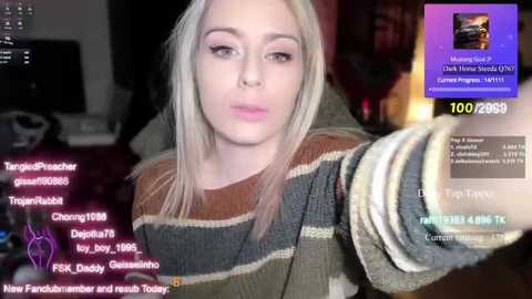 Media: A video of a blonde woman in a striped sweater, holding a phone, with text overlay showing comments and stats on a live stream.