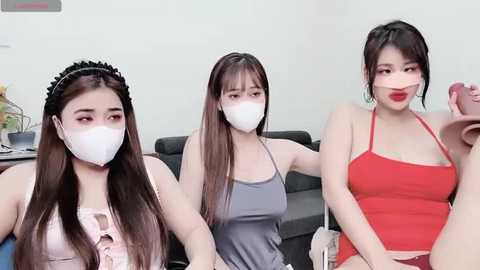 Media: Video of three Asian women with long black hair, wearing face masks, in casual clothes, seated in a modern living room.