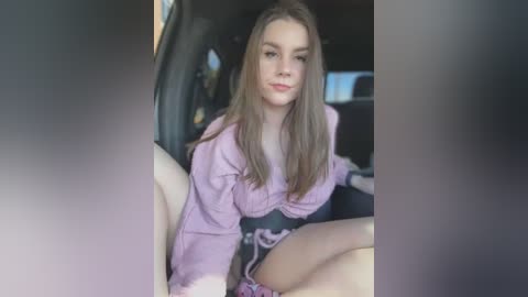 Media: Video of a young woman with long, straight, light brown hair, wearing a lavender hoodie and black shorts, sitting in a car seat.