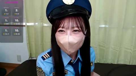 Media: Video of a young East Asian woman wearing a blue police uniform, mask, and cap, smiling slightly, with a calendar behind her.