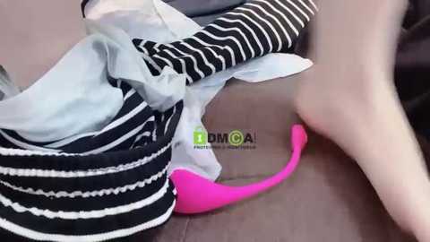 Media: A close-up video of a person wearing a striped black and white shirt, a pink bra, and a black skirt, lying on a brown surface.