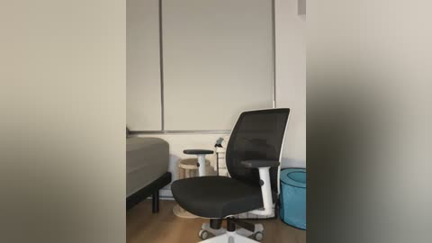 Video of a modern, minimalist medical exam room with a black mesh ergonomic chair, a small wooden table, and a blue plastic waste bin.