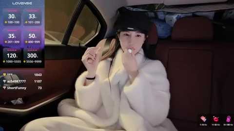 Media: Video of a young Asian woman wearing a black beanie and a white fur coat, sitting in the backseat of a car, eating a sandwich, with a live stream overlay showing her stats.