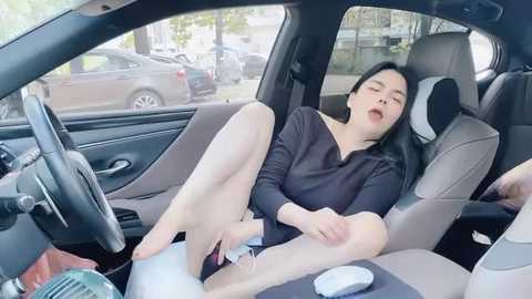 Media: Video of an Asian woman in a car, with long black hair, wearing a black top, white shorts, and white sneakers, lying on the backseat with her legs spread, masturbating, surrounded by a cluttered interior.