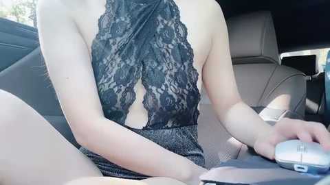 Media: Video of a light-skinned woman in a black lace halter top and short skirt, sitting in a car with a silver mouse on her lap.